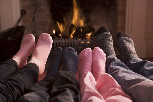 A group of feet in colorful socks resting in front of a cozy fireplace.