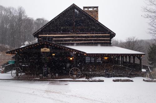 A rustic wooden building covered in snow, with festive lights and a snowy landscape in the background.