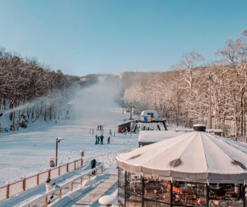 A snowy landscape with a ski slope, people enjoying winter activities, and a cozy building in the foreground.