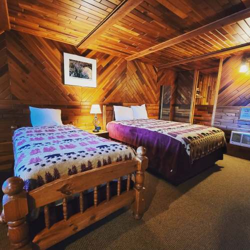 Cozy wooden cabin bedroom with two beds, warm lighting, and rustic decor.