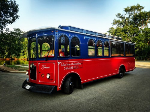 A colorful red and blue trolley bus parked near a scenic area, featuring large windows and a vintage design.