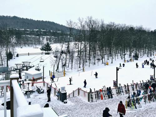 A snowy ski resort scene with skiers, a ski lift, and trees in the background.