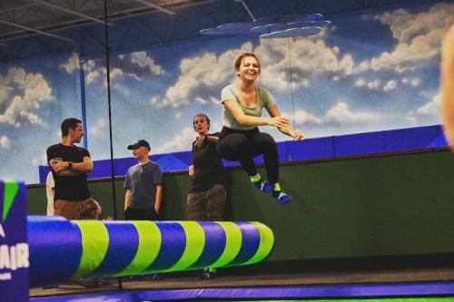 A group of people at a trampoline park, with one person joyfully jumping in the foreground.