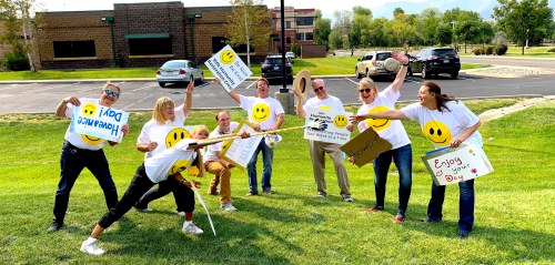A group of people in smiley face shirts holding signs and posing playfully in a grassy area.