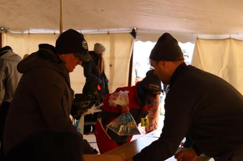 People sorting and distributing items inside a large tent, wearing winter clothing.