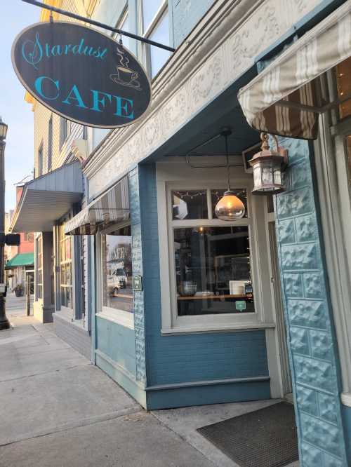 Exterior of Stardust Cafe, featuring a blue facade, hanging sign, and a welcoming entrance with a lantern.