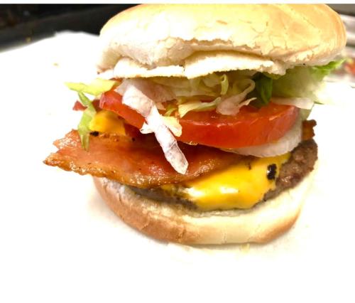 A close-up of a hamburger with lettuce, tomato, cheese, bacon, and a chicken patty in a soft bun.
