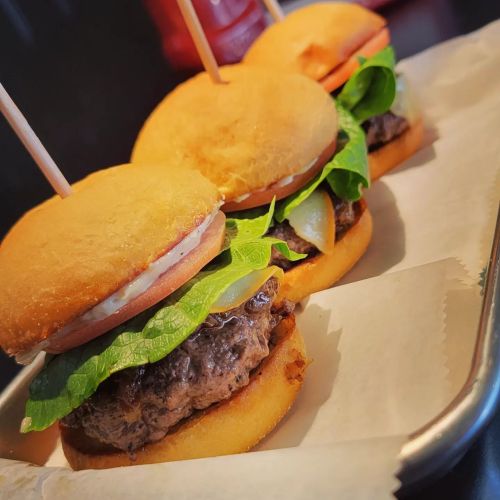 Three mini burgers with lettuce, tomato, and sauce, served on a tray with toothpicks.