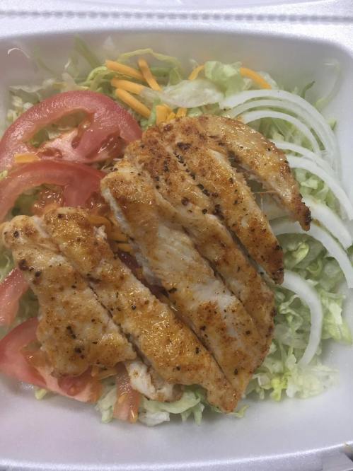 Grilled chicken strips on a bed of lettuce, topped with tomato, cheese, and onion slices.