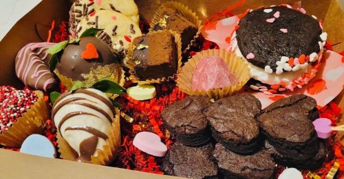 A box of assorted Valentine's Day treats, including cookies, brownies, chocolate-covered strawberries, and heart-shaped candies.