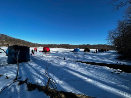 People ice fishing on a frozen lake, with colorful tents set up against a clear blue sky.