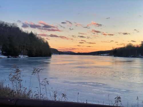 A serene river at sunset, with icy water and trees lining the banks under a colorful sky.