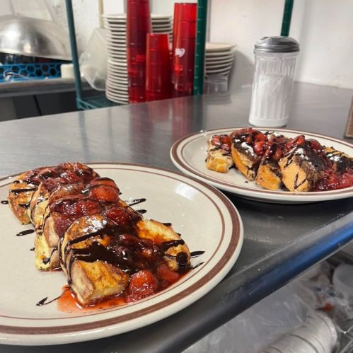 Two plates of French toast topped with strawberries, chocolate drizzle, and powdered sugar, on a kitchen counter.