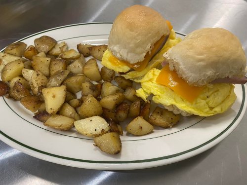 A plate with two breakfast sandwiches and a side of golden-brown, seasoned potato cubes.
