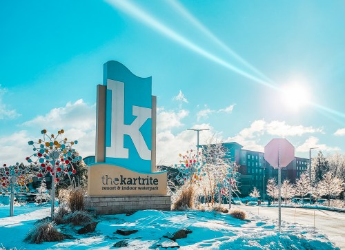 Sign for The Kartrite Resort and Indoor Waterpark, surrounded by snow and colorful decorations, under a bright blue sky.