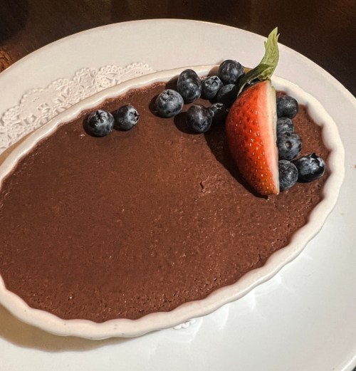 A chocolate dessert on a white plate, garnished with blueberries and a strawberry.