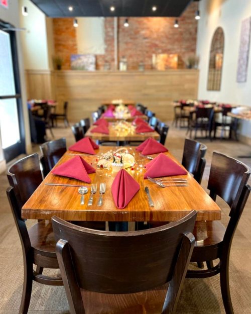 A dining area with a long wooden table set with maroon napkins and silverware, surrounded by dark wooden chairs.