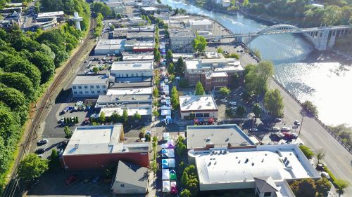 Aerial view of a riverside town with buildings, trees, and colorful tents set up along the street.