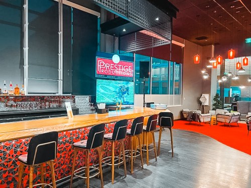 A modern bar area with high stools, a vibrant sign reading "Prestige Productions," and stylish decor.