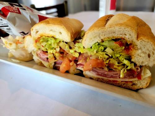 A close-up of a sandwich filled with lettuce, tomato, and layers of deli meats, served on a white plate.
