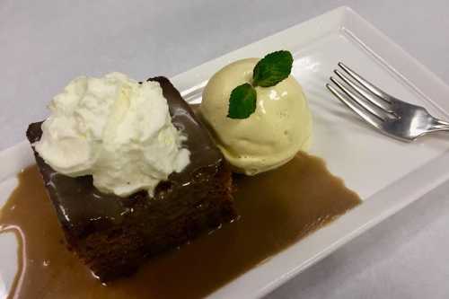 A slice of chocolate cake topped with whipped cream, served with a scoop of vanilla ice cream and a mint leaf garnish.