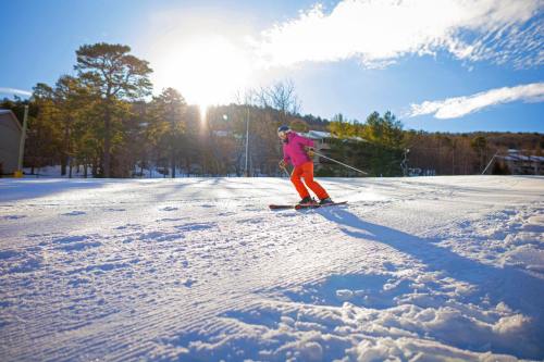 A skier in bright pink and orange gear glides down a snowy slope under a sunny sky.
