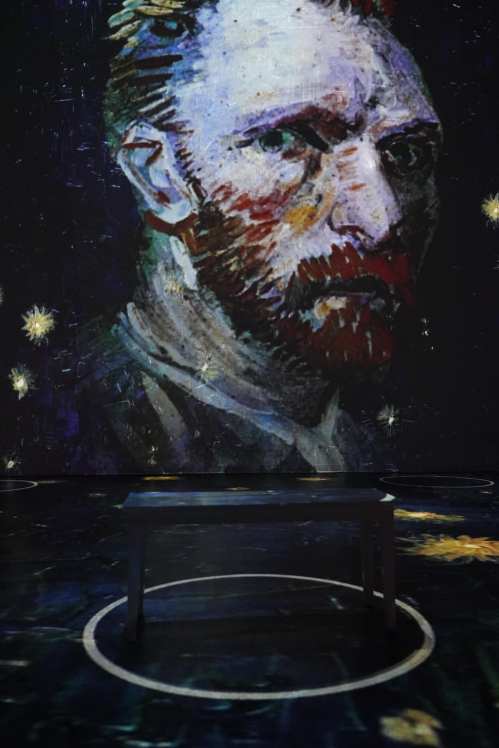 A vibrant projection of Vincent van Gogh's self-portrait on a dark wall, with a table in the foreground.