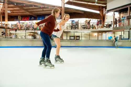 Two young women ice skating together on a rink, smiling and enjoying their time.