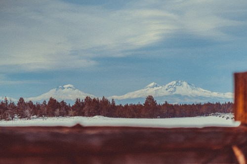 Snow-capped mountains rise above a forested landscape under a blue sky with wispy clouds.