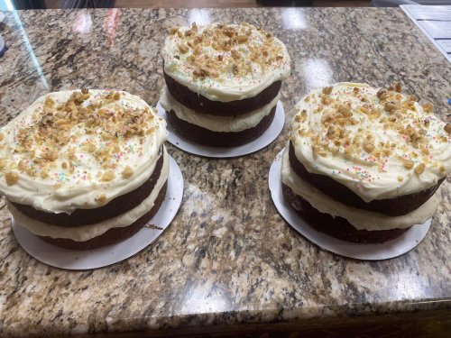 Three layered cakes with cream frosting and chopped nuts, displayed on a granite countertop.