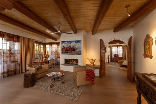 Cozy interior of a stylish room featuring a fireplace, wooden beams, and warm decor with a dining area and bedroom visible.
