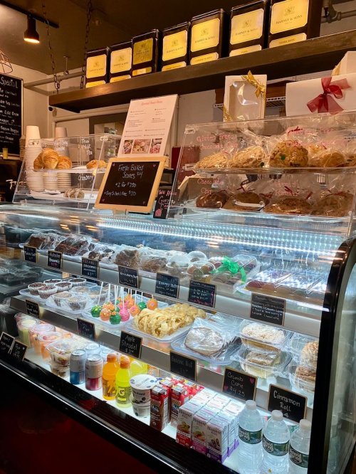 A display case filled with various baked goods, cookies, and drinks, with a menu board above.