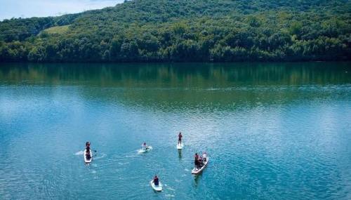 Aerial view of people paddleboarding on a calm lake surrounded by lush green hills.