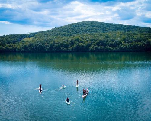 Aerial view of people paddleboarding on a calm lake surrounded by lush green hills under a cloudy sky.