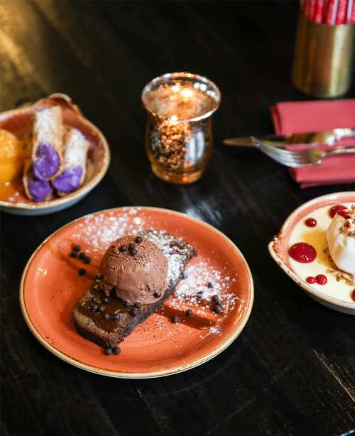 A colorful dessert spread featuring chocolate cake with ice cream, sweet rolls, and a decorative candle.