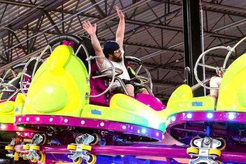 A person with arms raised enjoys a colorful amusement park ride, surrounded by vibrant lights and playful designs.