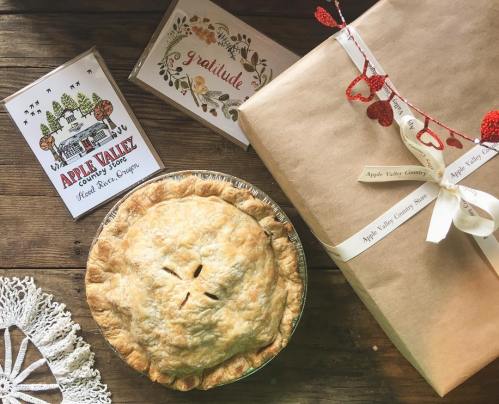 A freshly baked apple pie next to a wrapped gift and greeting cards, set on a rustic wooden table.