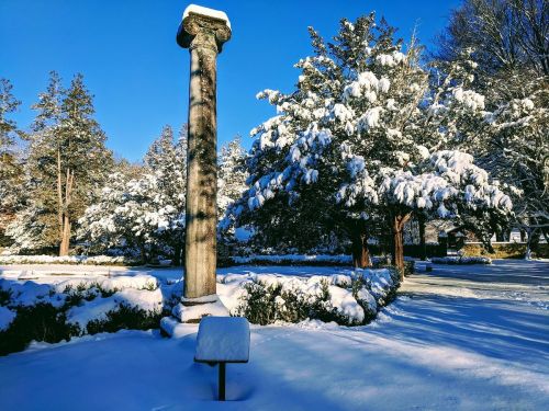 A snow-covered landscape featuring a tall stone column surrounded by trees and a blanket of fresh snow.