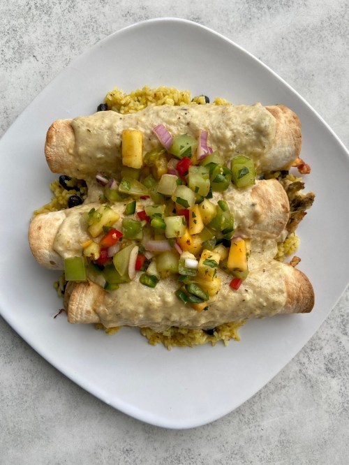 Three enchiladas topped with salsa on a bed of yellow rice and black beans, served on a white plate.