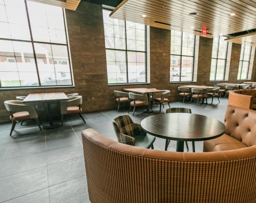 Modern restaurant interior featuring wooden tables, upholstered chairs, and large windows.