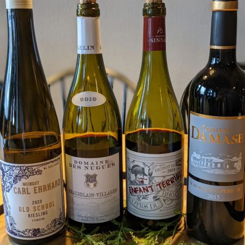 Four wine bottles displayed on a wooden table, featuring labels from Carl Ehrhard, Domaine des Nugues, and Château Damase.