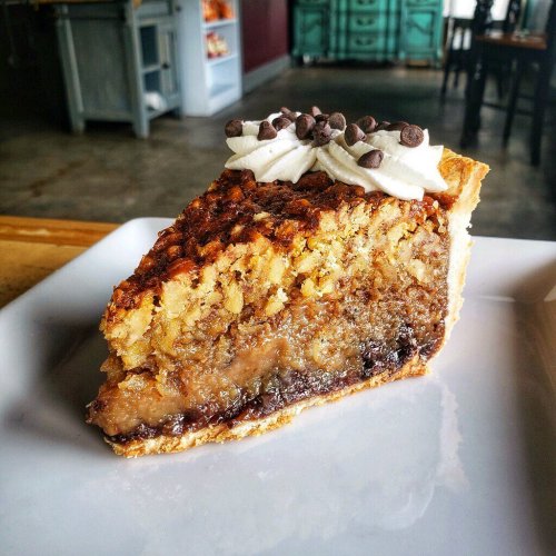 A slice of pie with a golden crust, topped with whipped cream and chocolate chips, showcasing a layered filling.