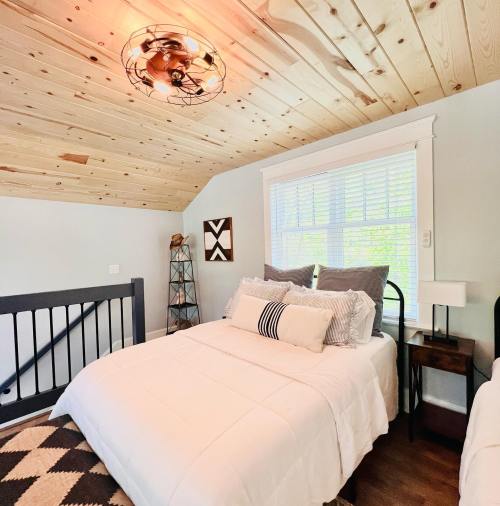 Cozy bedroom with a wooden ceiling, a bed with decorative pillows, and a window letting in natural light.