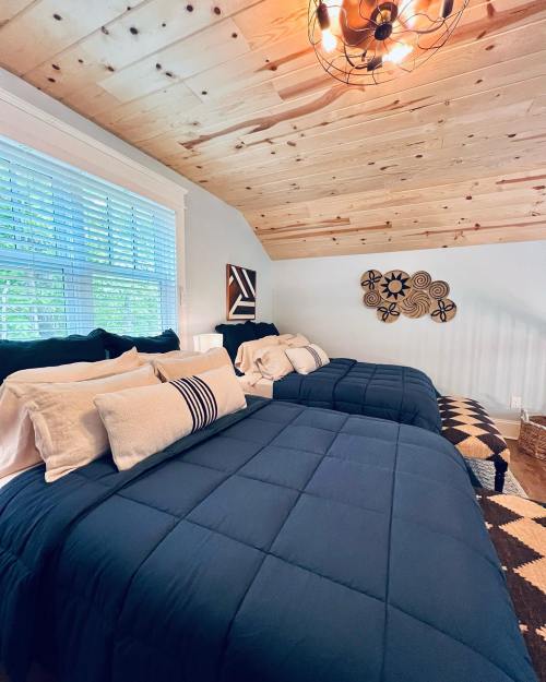 Cozy bedroom with two beds, wooden ceiling, and decorative wall art, featuring blue bedding and natural light.