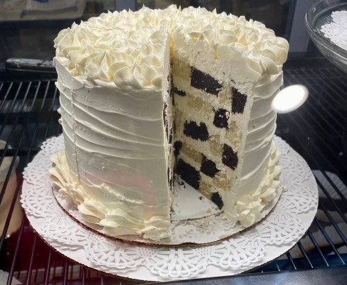 A round cake with white frosting, partially sliced to reveal layers of chocolate and vanilla cake inside.