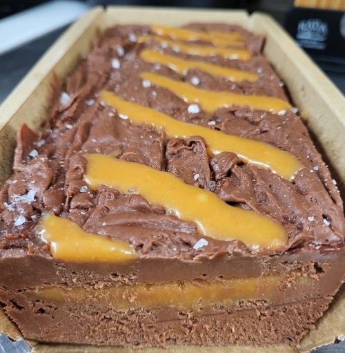 A rectangular chocolate dessert with a smooth caramel drizzle and a sprinkle of salt on top.