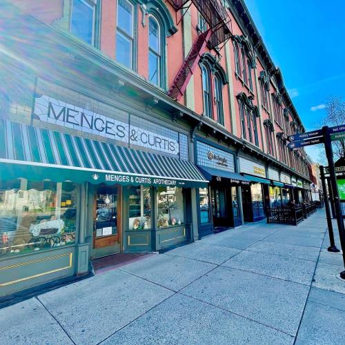 A street view of a historic building with shops, including Menges & Curtis Apothecary, under a clear blue sky.