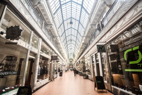 A spacious, well-lit shopping arcade with glass ceilings and storefronts on either side.