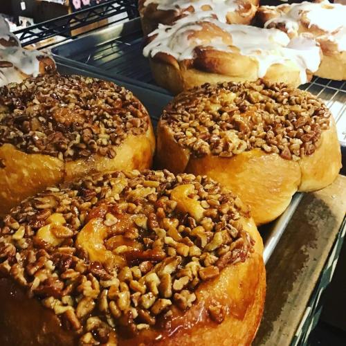 Freshly baked cinnamon rolls topped with nuts and icing, displayed on a cooling rack.