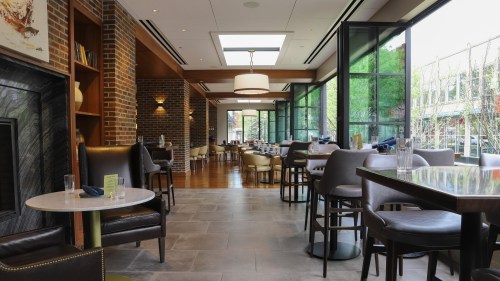 Modern restaurant interior featuring large windows, wooden accents, and a mix of seating arrangements.
